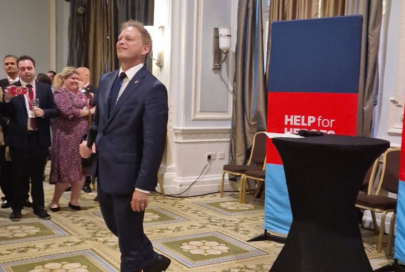 Grant Shapps with microphone in front of Help for Heroes banner